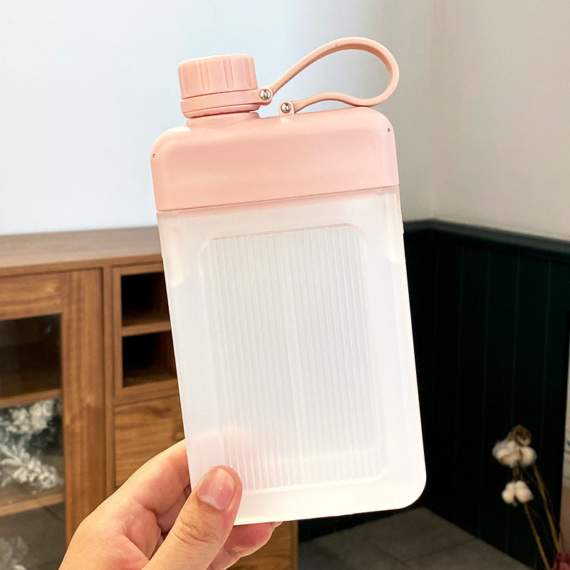 Pink flat square water bottle held by a hand against a blurred background