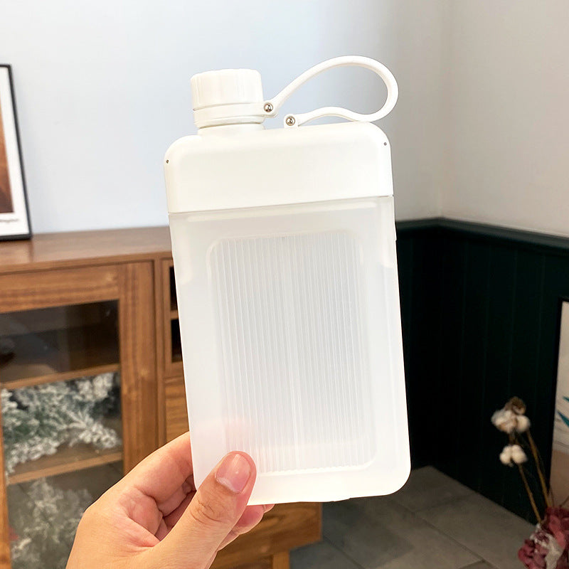 White capped flat square water bottle hand with a blurred indoor background