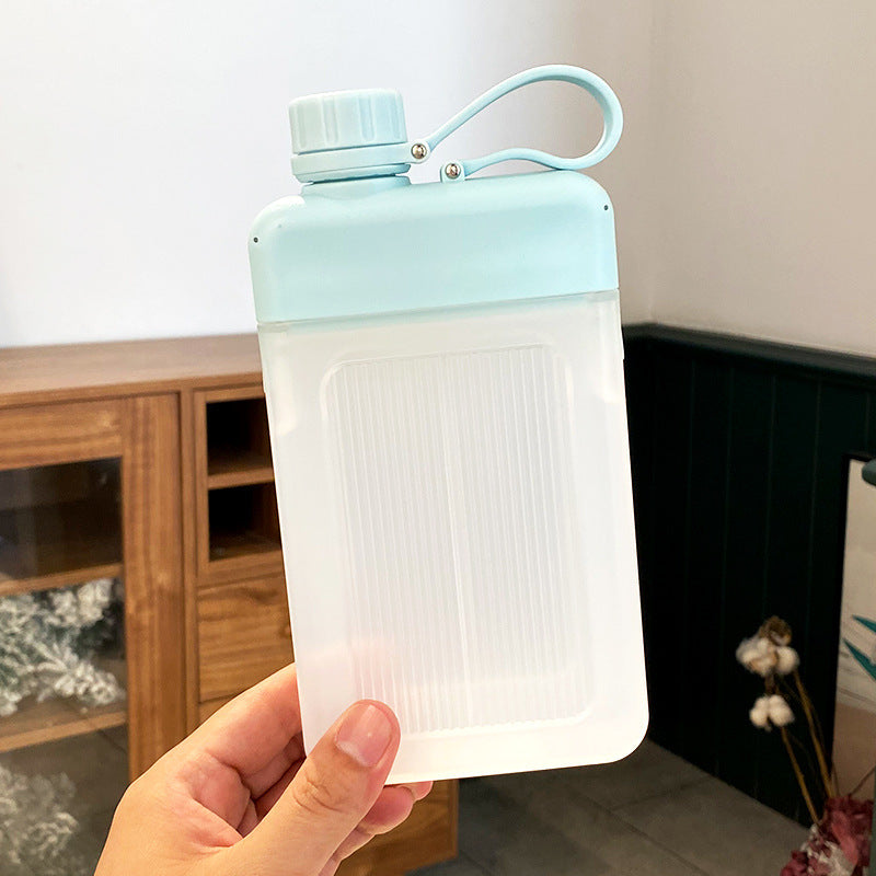 Light blue and clear flat square water bottle held in a hand with a neutral background