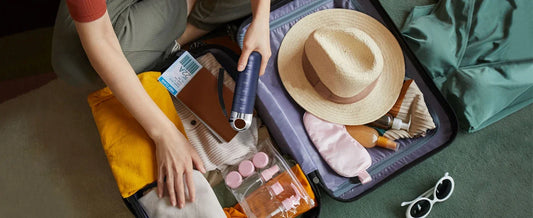 Person packing a suitcase with travel items including a hat, sunglasses, and toiletries.