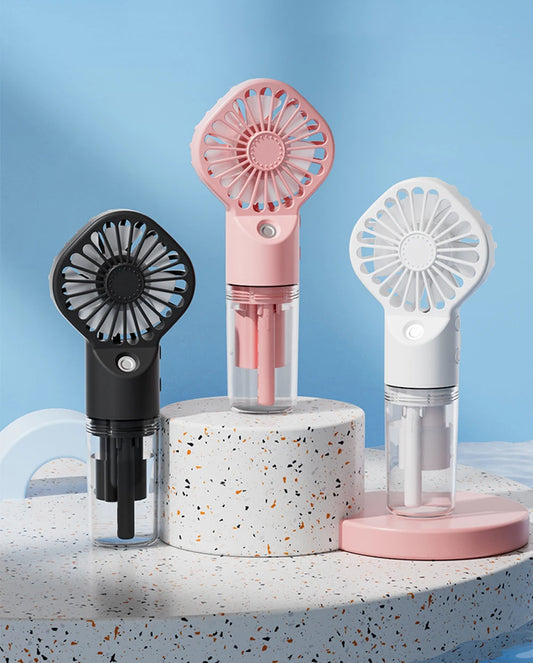Three portable fans in black, pink, and white on a speckled surface with a blue gradient background.