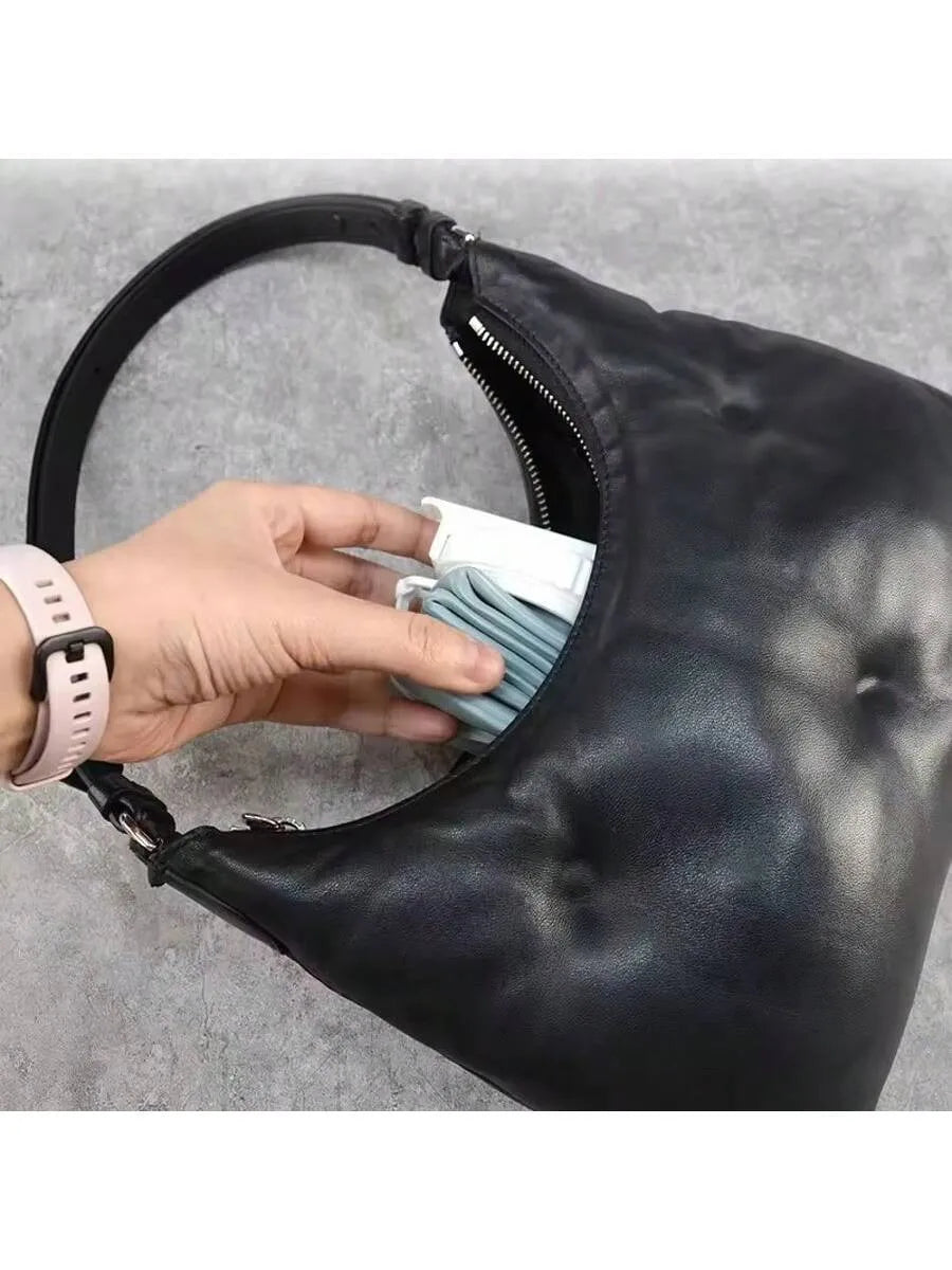 Person placing the folded bottle in a black leather handbag with a gray background