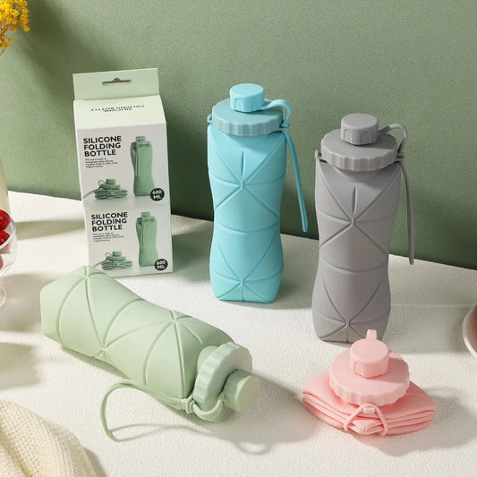 All the available Collapsible Silicone Water Bottles sat on a table. available in colours are Grey, Blue, Green and Pink all light pastel colours.