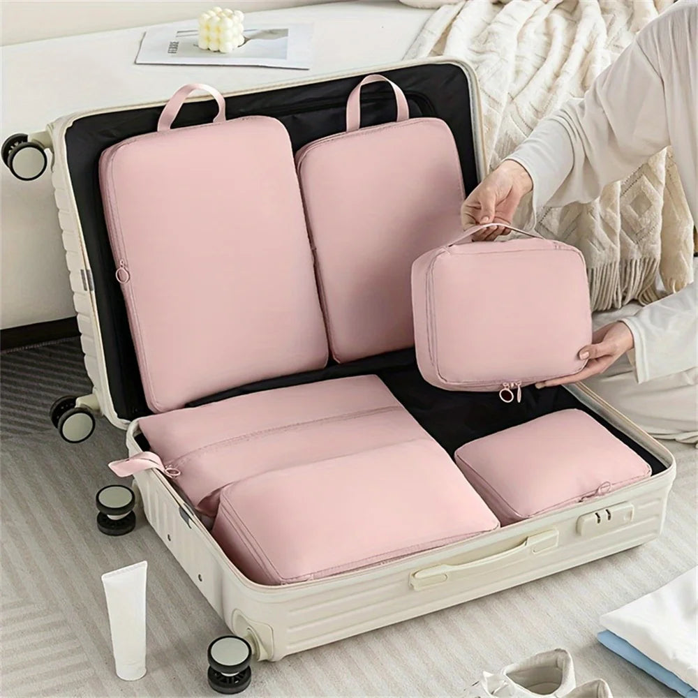 Person packing pink travel cubes into an open suitcase on a bed.