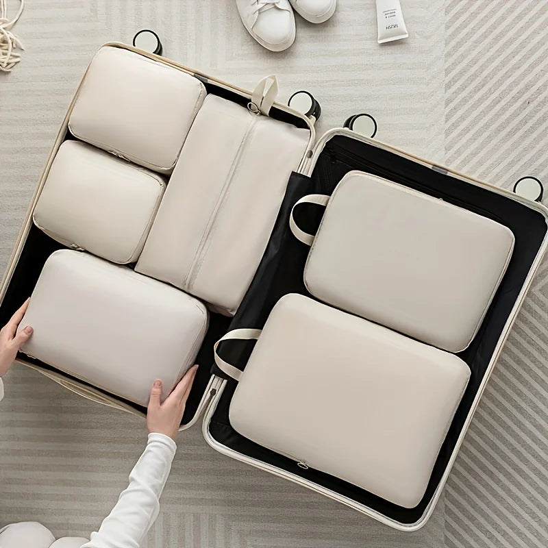 Person packing white travel packing compression cubes into a suitcase on a light wooden floor.