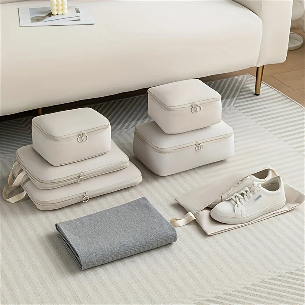 Set of beige packing cubes and gray blanket on a light wooden floor with a white couch in the background.
