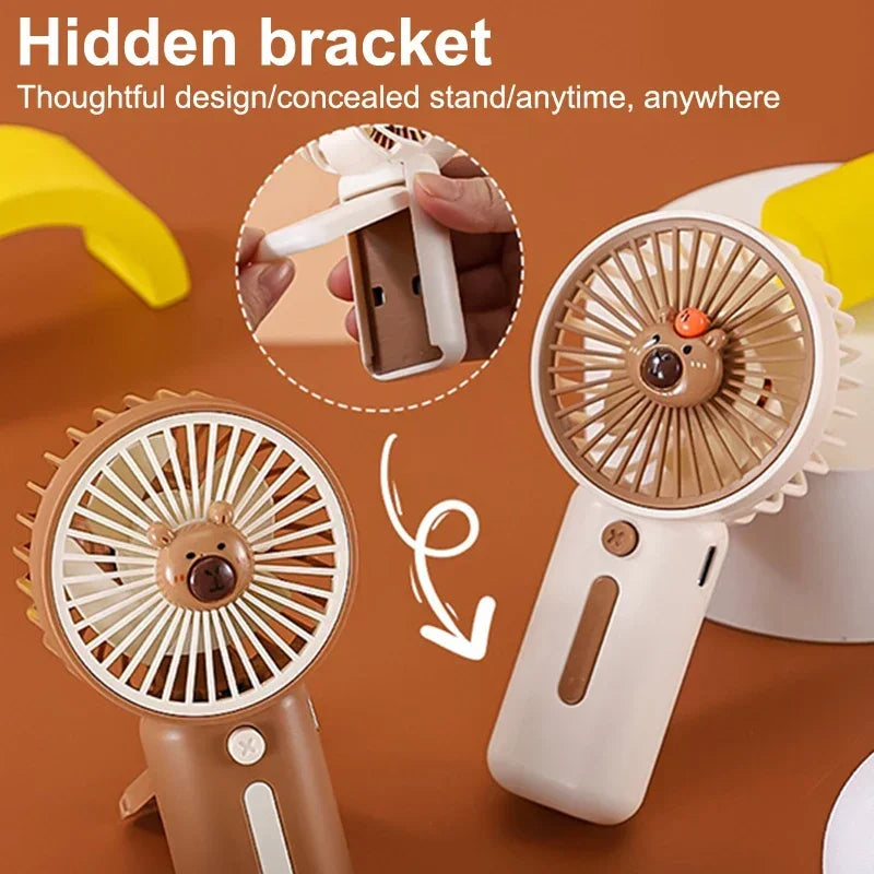 Compact Capybara-themed handheld USB fan one is white the other brown there is a picture within the picture showing that the back of the fan can be pulled out so the fan can stand up on a table.