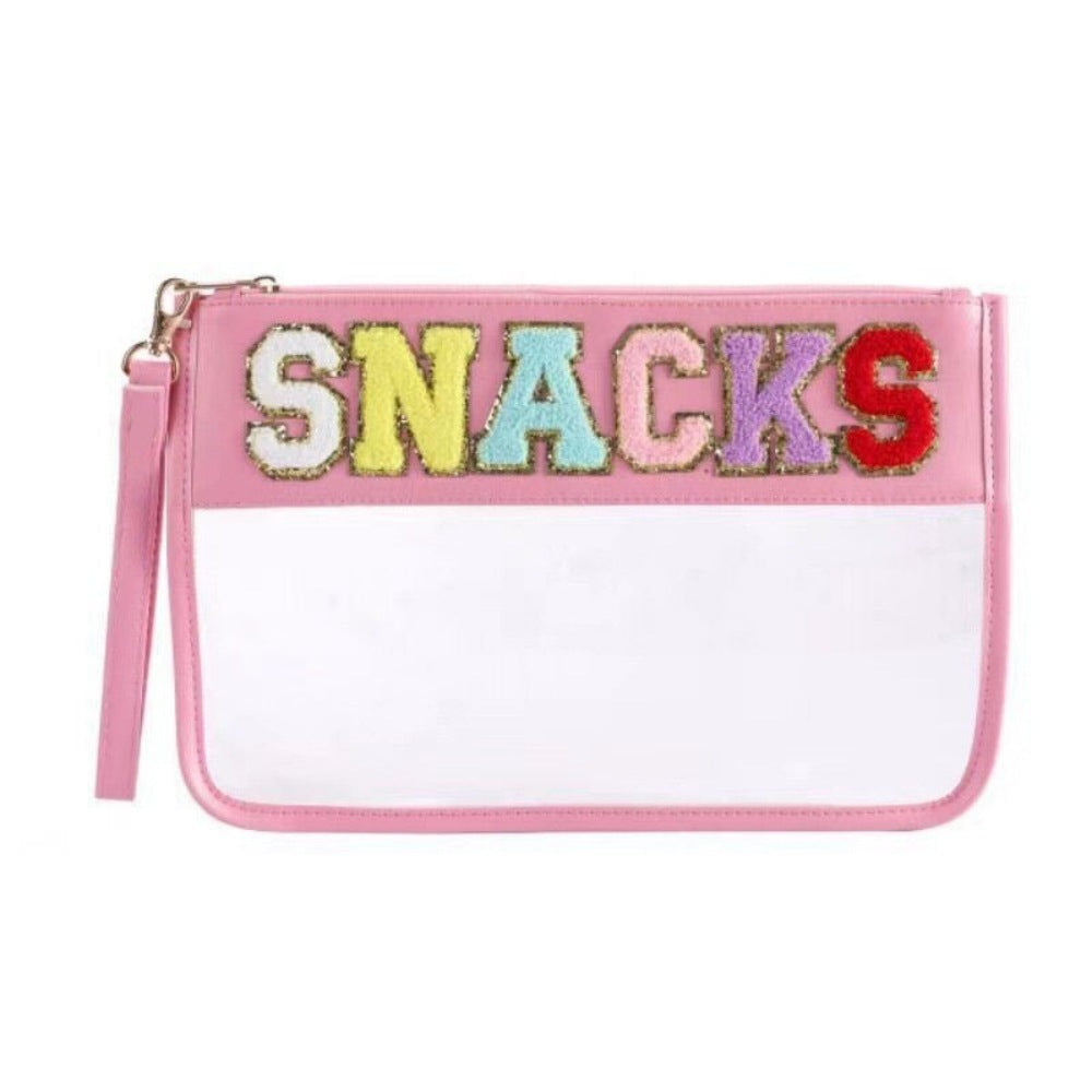 white background and in the foreground a clear and transparent
Pink lined pouch bag with the word snacks across the top in colourful letters that are lined with glittery gold. There is a wrist strap attached to the zipper of the snack bag that matches the pink lining of the bag.