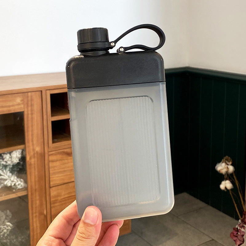 Person holding a black capped flat water bottle with a wooden cabinet in the background