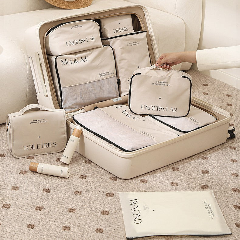 Cream suitcase open next to cream sofa. showing the 8 piece set and a lady in a cream suit is holding the underwear cube to show that its different from the underwear bag.