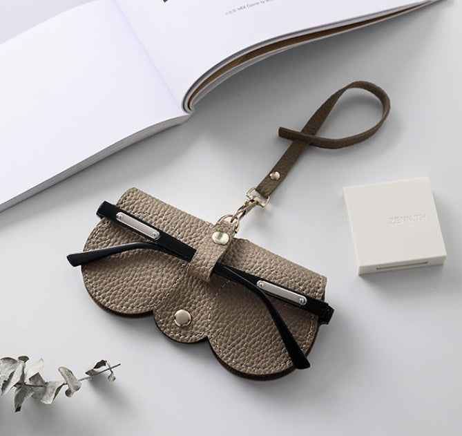 Beige clip on glasses holder on a white table, with glasses in the holder ready to be clipped on the bag. A great travel glasses case.