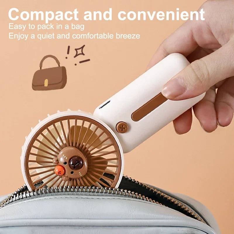 white Compact Capybara-themed handheld USB fan being packed into a light grey bag – perfect for travel or theme park use