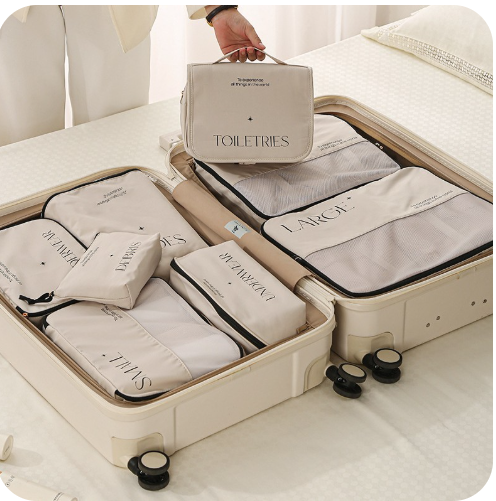 This is an open suitcase of the 8 piece set and a female in a cream suit is holding the toiletries bag over the suitcase.