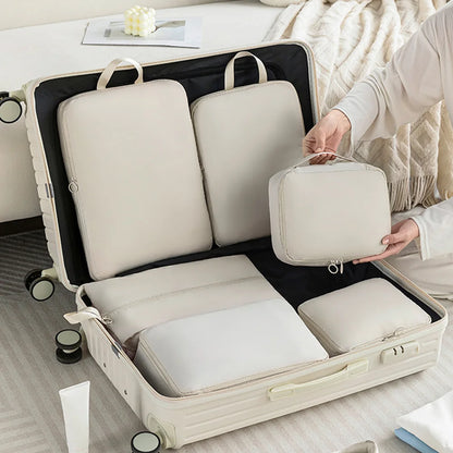 Person packing a suitcase with beige (white) travel bags on a bed.