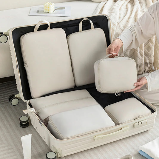 Person packing a suitcase with beige (white) travel bags on a bed.