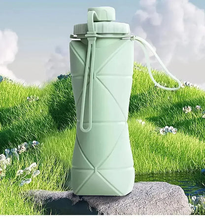 Pastel Green Collapsible Silicone Water Bottle, sat on a rock in the middle of a green medow