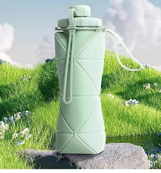 Pastel Green Collapsible Silicone Water Bottle, sat on a rock in the middle of a green medow