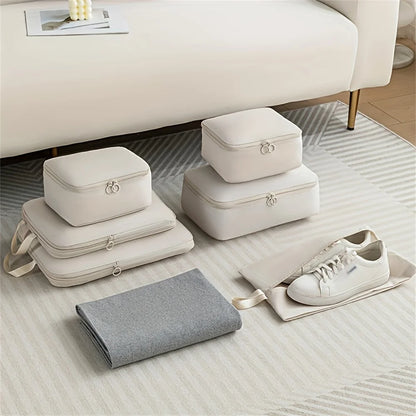 Set of beige packing cubes and gray blanket on a light wooden floor with a white couch in the background.