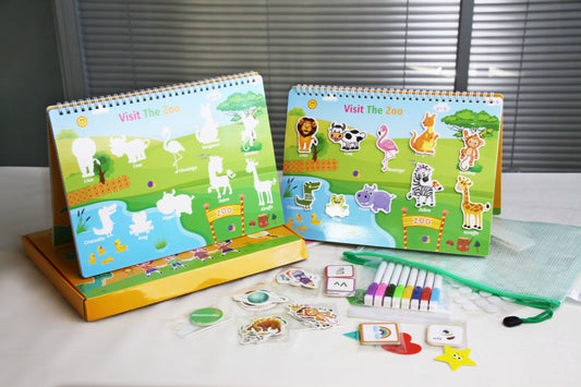 The busy book is open to the match the zoo animals to the spaces in the picture page. the busy book is stood up on the table and next to it is animal cards, coloured pens the storage box and bag.
