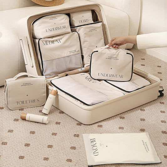 Cream suitcase open next to  cream sofa. showing the 8 piece set and a lady in a cream suit is holding the underwear cube to show that its different from the underwear bag. 
