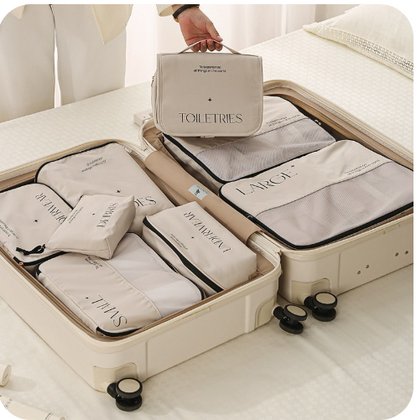 This is an open suitcase of the 8 piece set and a female in a cream suit is holding the toiletries bag over the suitcase.